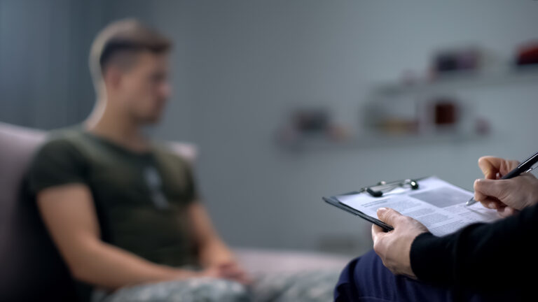 Psychologist making notes during therapy session with sad male s