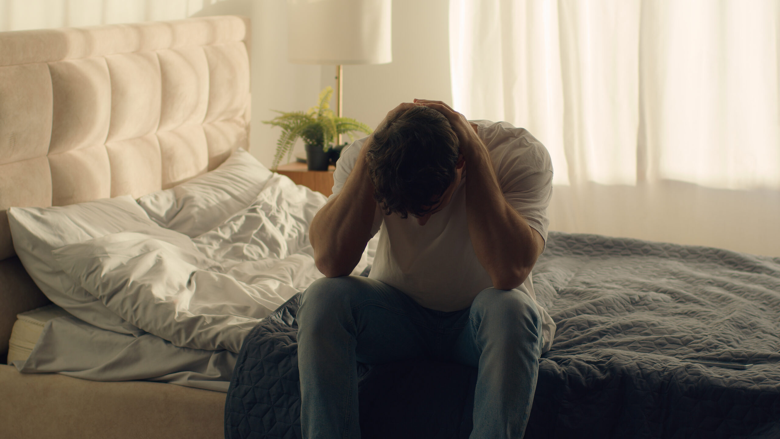 young man sitting on bed in grief.