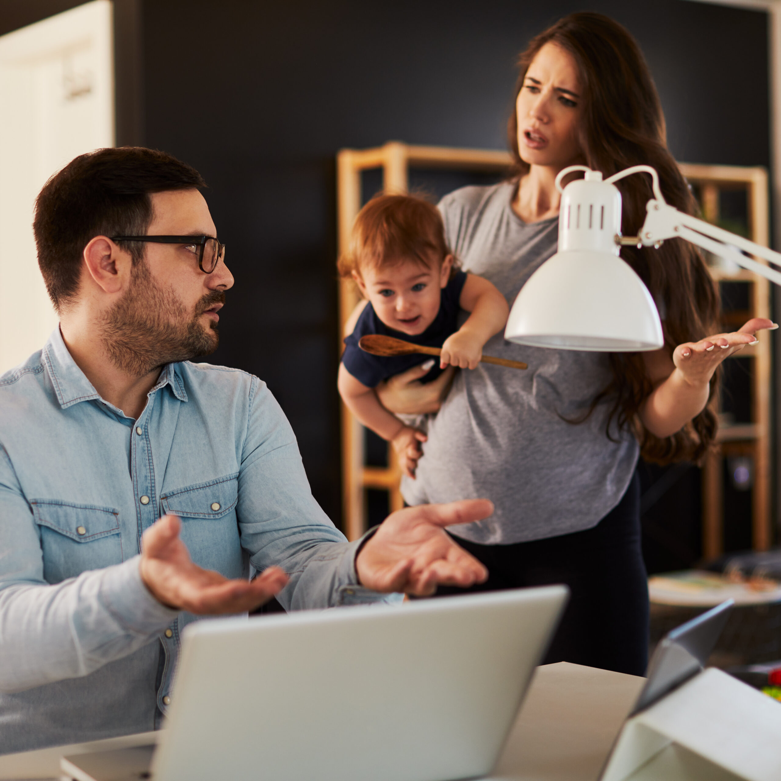 Married Couple in an argument while husband works and wife holds baby.