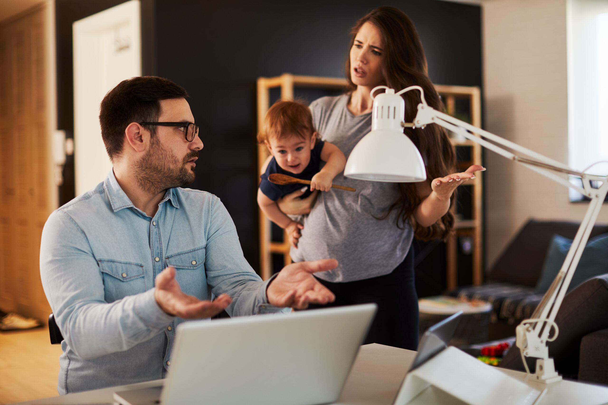 Young family couple arguing at home husband working and the woman holds the child and complains to him