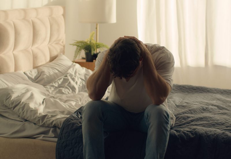 young man sitting on bed in grief.