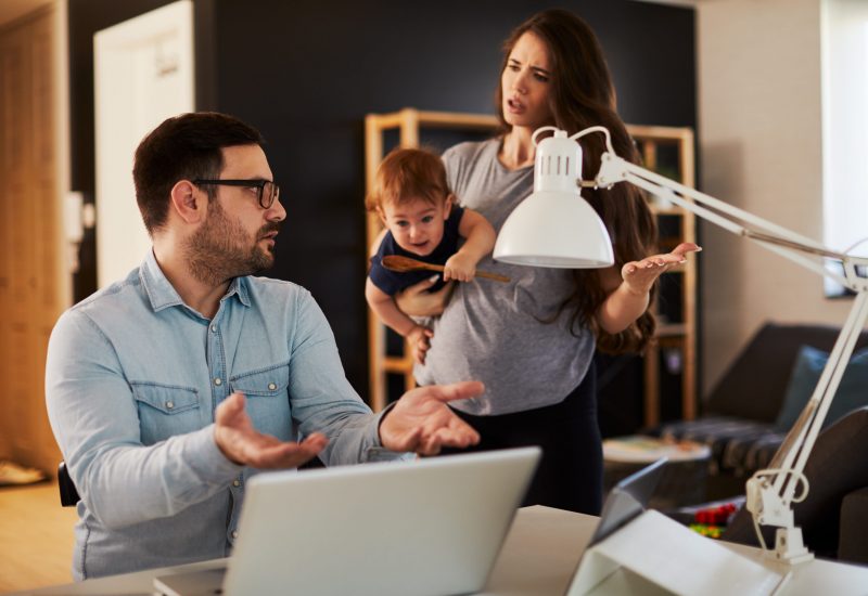 Young family couple arguing at home husband working and the woman holds the child and complains to him